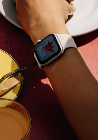 En person tager et stykke mad fra en tallerken, Apple Watch SE 3 på håndleddet, urkasse i aluminum i farven stjerneskær, altid aktiv-skærm, urskiven viser et portræt af en person, Sportsrem i farven stjerneskær