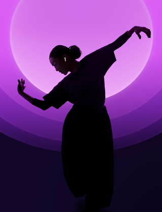 En person danser med AirPods 5 i ørerne mod en baggrund med flere farver